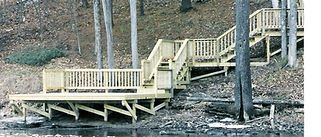 Wooden deck and staircase built on a slope, leading from the water's edge into the trees.