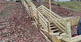 Wooden staircase with handrails built on a hillside, connecting different levels.