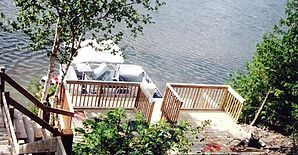 Wooden decks and boat on lake, accessible by stairs. Green trees frame the water.