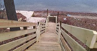 Wooden boardwalk with railings leads to a beach and water.