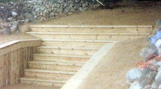 Wooden outdoor staircase built into a sand-colored hillside.