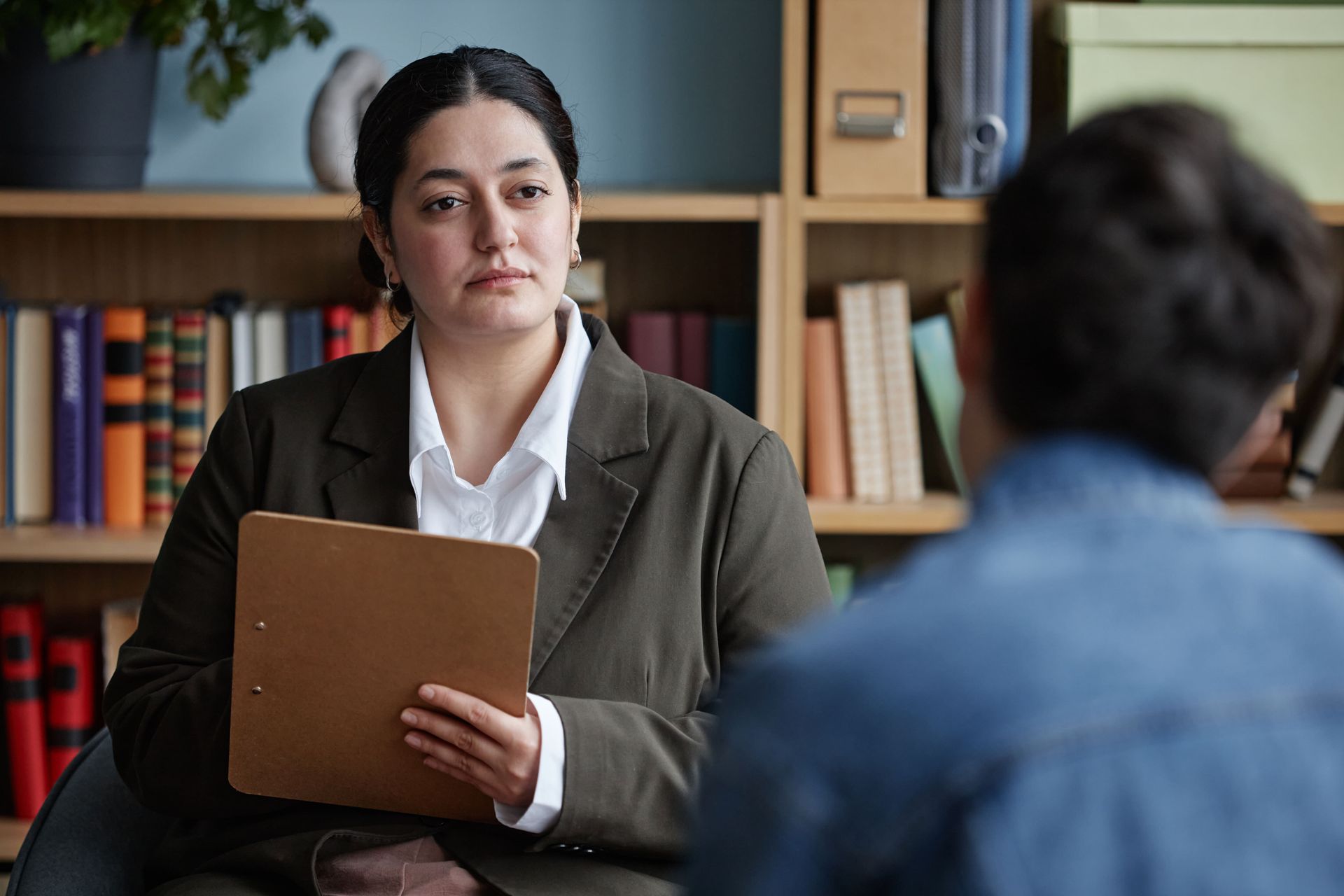 Woman with short gray hair, wearing glasses and black blazer, holds a pen and notebook, looking to the side.