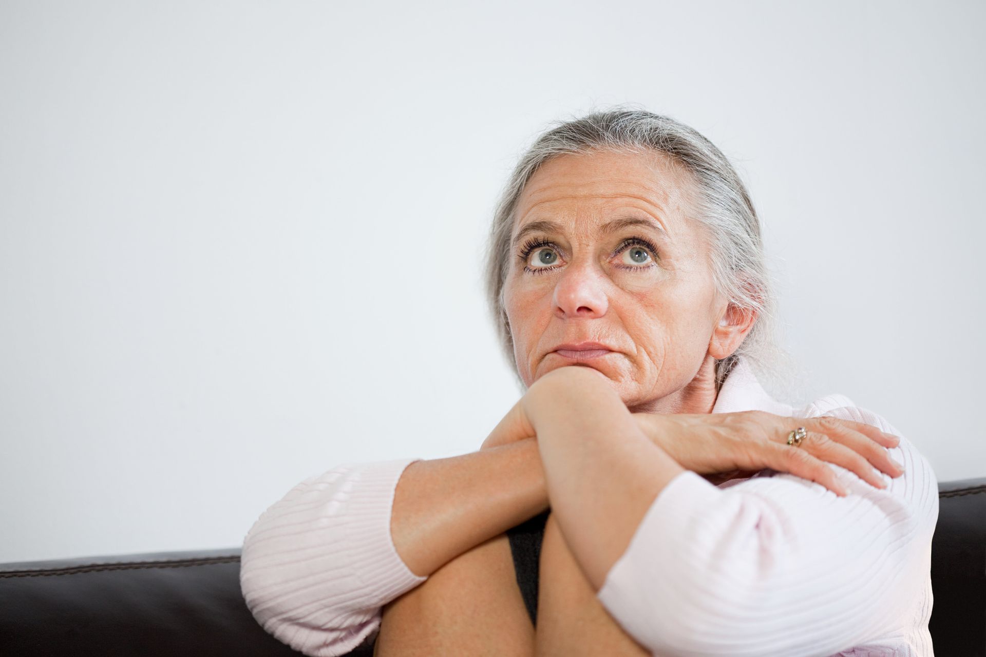 Woman with gray hair looking upwards, arms crossed, thoughtful expression.