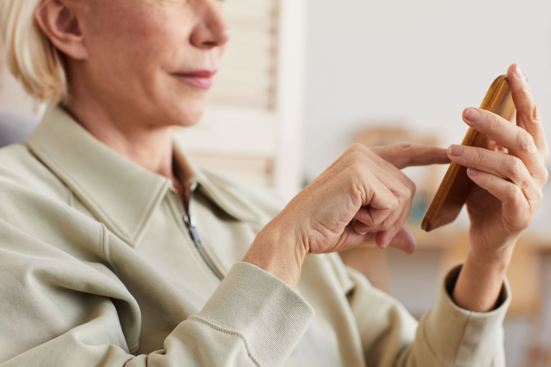 Woman using a smartphone, tapping the screen with her finger. She is wearing a light green jacket.