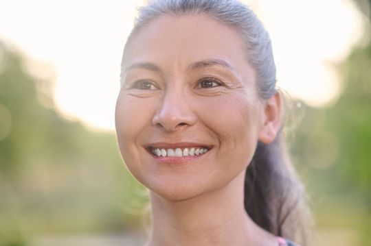 Woman with gray hair smiles outdoors.