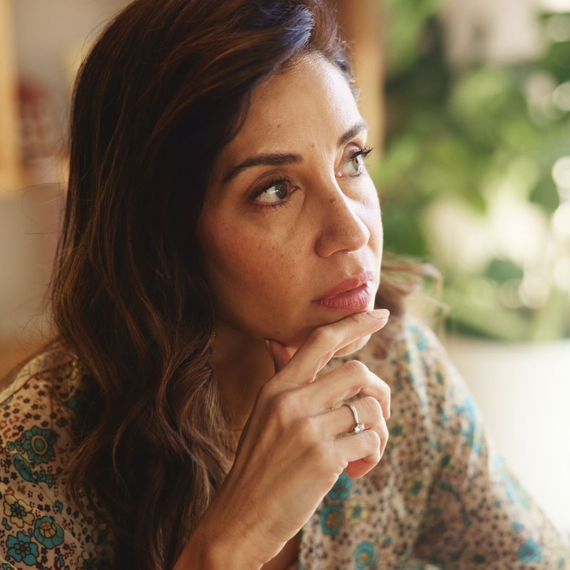 Woman with brown hair, resting chin on hand, looking off to the side, wearing patterned top.