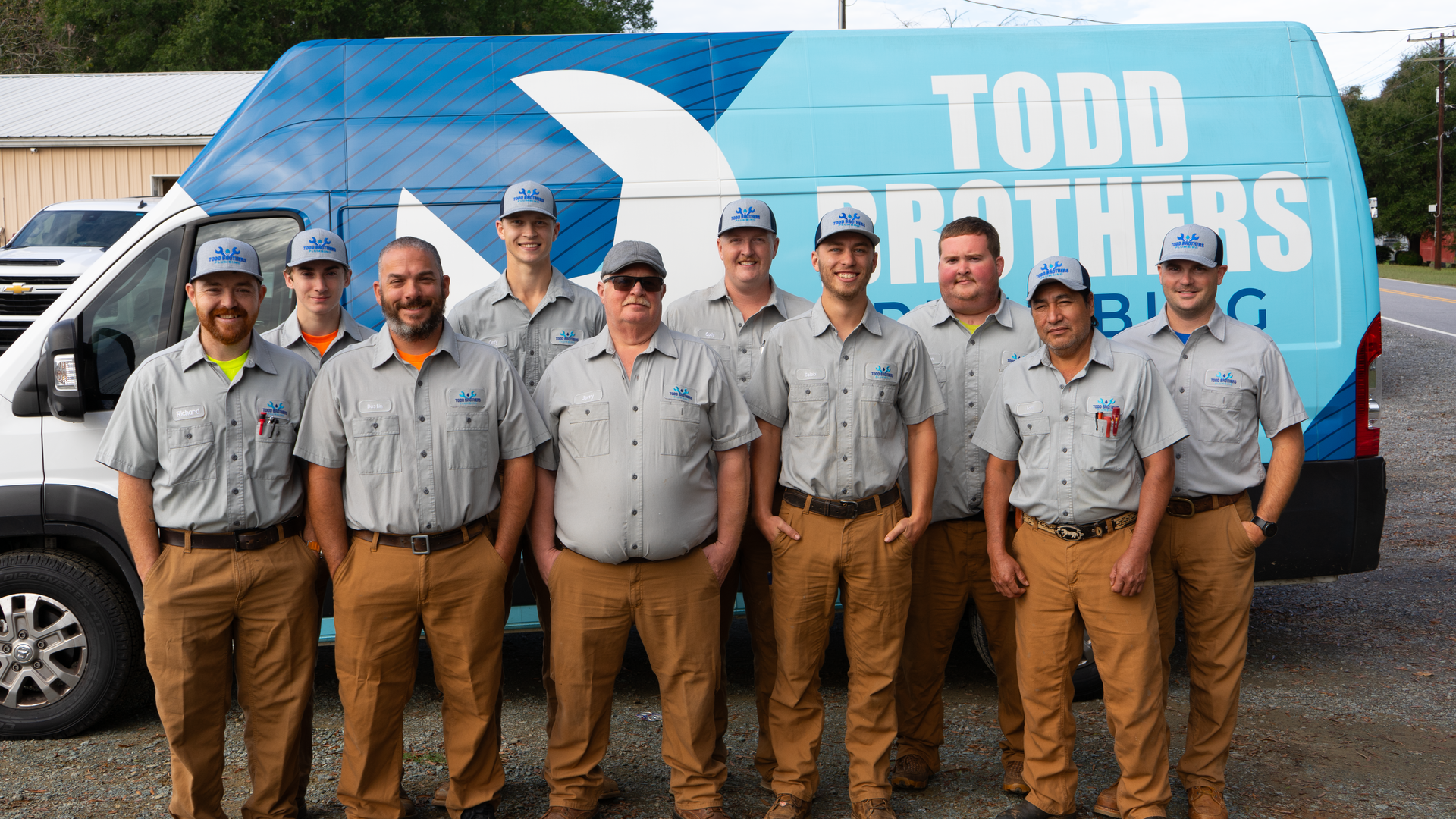 Group of men in work uniforms posing in front of a blue van that says 