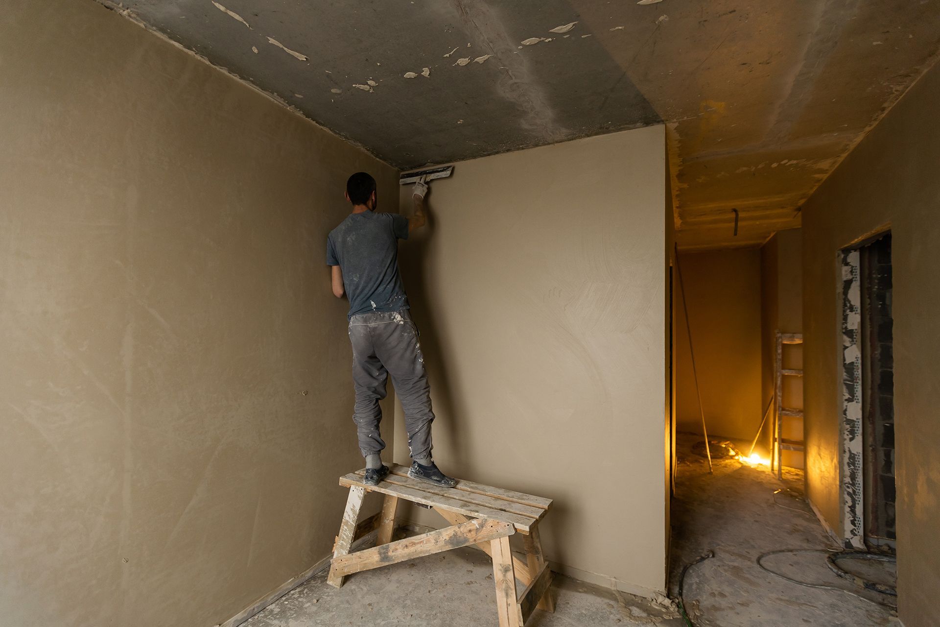 a man is plastering a wall while standing on a wooden bench