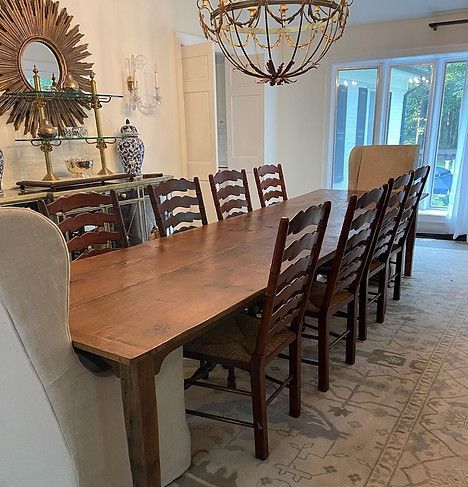 Dining room with long wooden table, ladder-back chairs, chandelier, and buffet with mirror