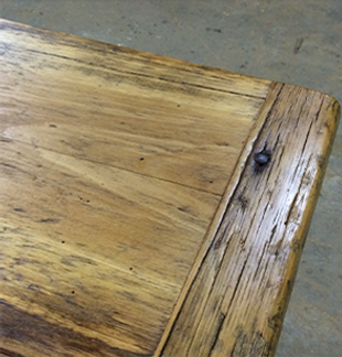 Close-up of a weathered wooden table corner with visible grain, fastened with a dark nail