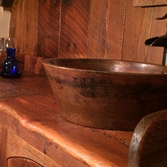 Rustic bathroom sink with a copper bowl, wood counter and paneling, and a blue glass bottle
