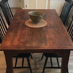 Wooden dining table with four black chairs; a decorative bowl and placemat sit on the table