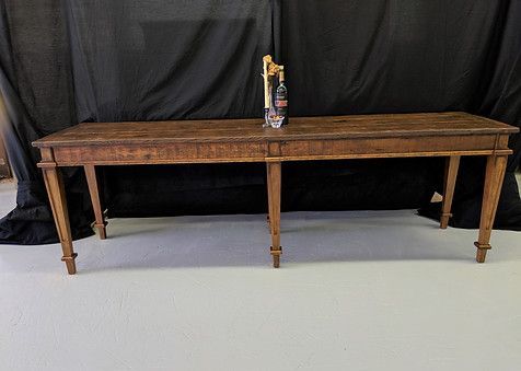 Long, wooden table with a tap and bottle on top; black backdrop