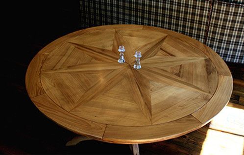 Round wooden table with inlaid starburst pattern, two glass candle holders