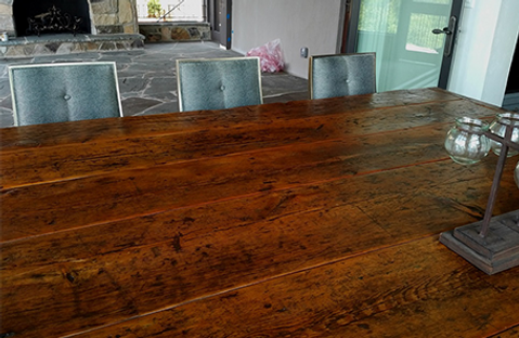 A large, rustic wooden dining table with three blue-upholstered chairs