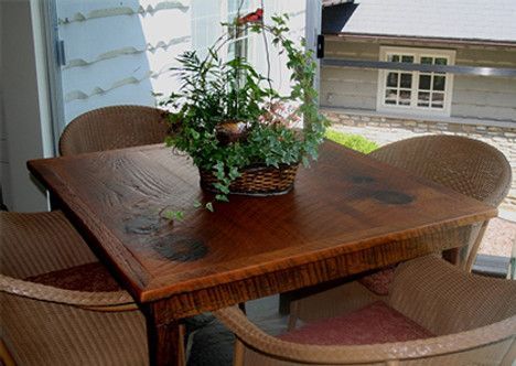 Square wooden table with a basket of plants, surrounded by wicker chairs, on a porch