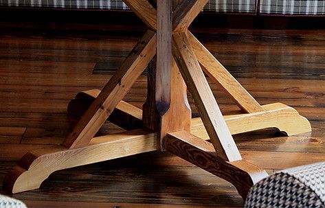 Wooden table base with crossed supports and rounded feet on a wood floor