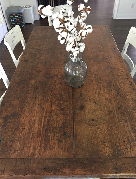 Wooden dining table with cotton stems in a glass vase; two white chairs are visible
