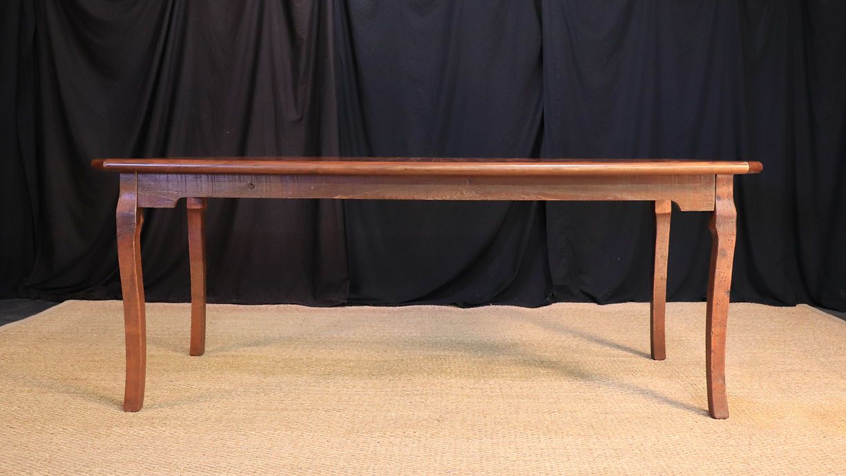 Wooden antique table with curved legs on a woven rug in front of a black background