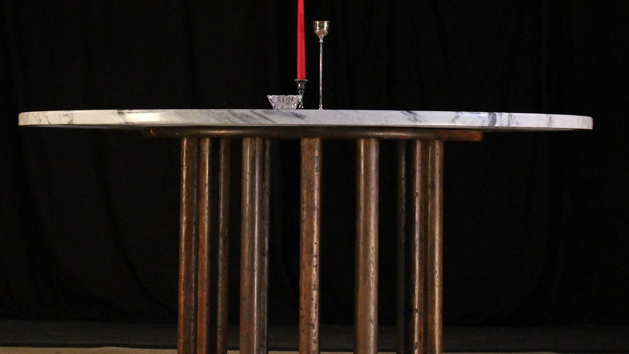 Table with marble top, brass legs, holding a red candle and glass objects against a black backdrop