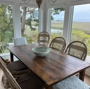 Wooden dining table with six chairs in a sunroom, overlooking a marsh