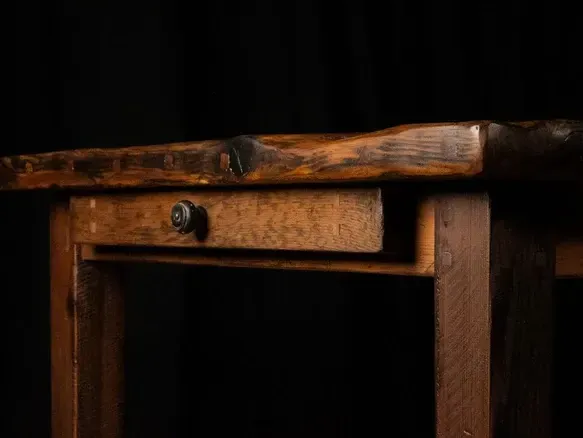 Wooden table with drawer, close-up against a black background, showing wood grain and a dark knob