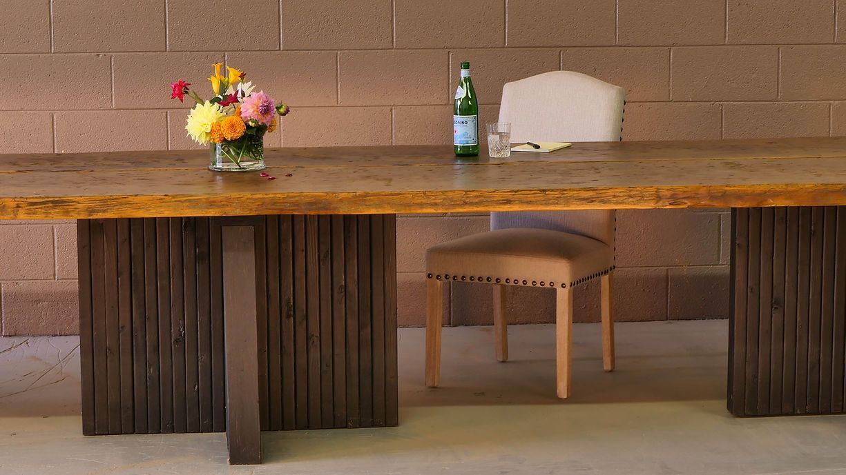 Dining table with wood base, flowers, water bottle, and beige chair against brick wall