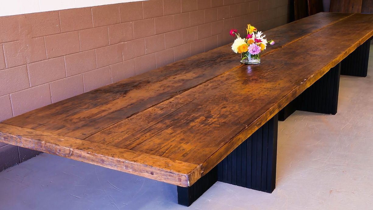 Long, rustic wooden table with a vase of flowers, set against a brick wall