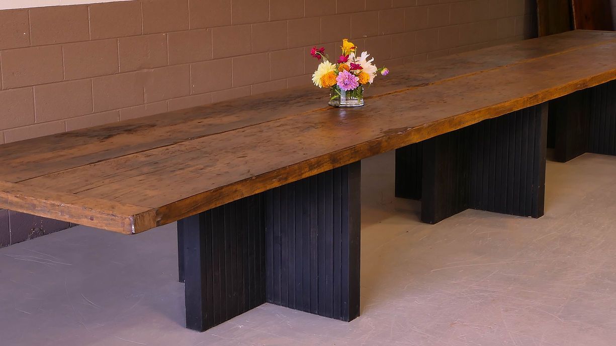 Long wooden table with black legs, topped with flowers, against a brick wall