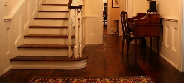 A hallway with stairs, dark wooden floors, and a desk