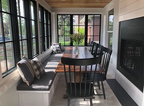 Sunroom with long wooden table, black chairs, built-in bench, black-framed windows, fireplace, and light wood ceiling