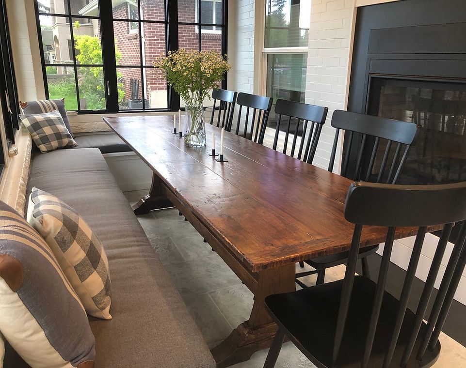 Dining room with large wooden table, bench seating, black chairs, flowers, and a fireplace