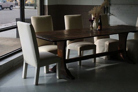 Dining table with cream chairs in a dimly lit room, a vehicle visible outside a window