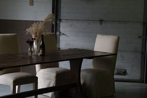 Dining table with chairs in a garage-like setting, featuring floral arrangements and a bottle