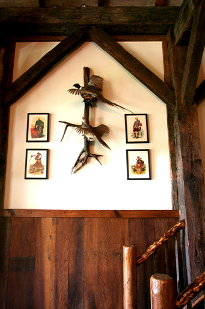 Rustic interior with mounted birds, framed art on a wood-paneled wall, framed by wooden beams