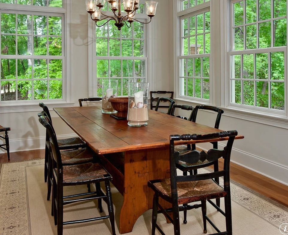 Dining room with wooden table, chairs, and windows overlooking greenery