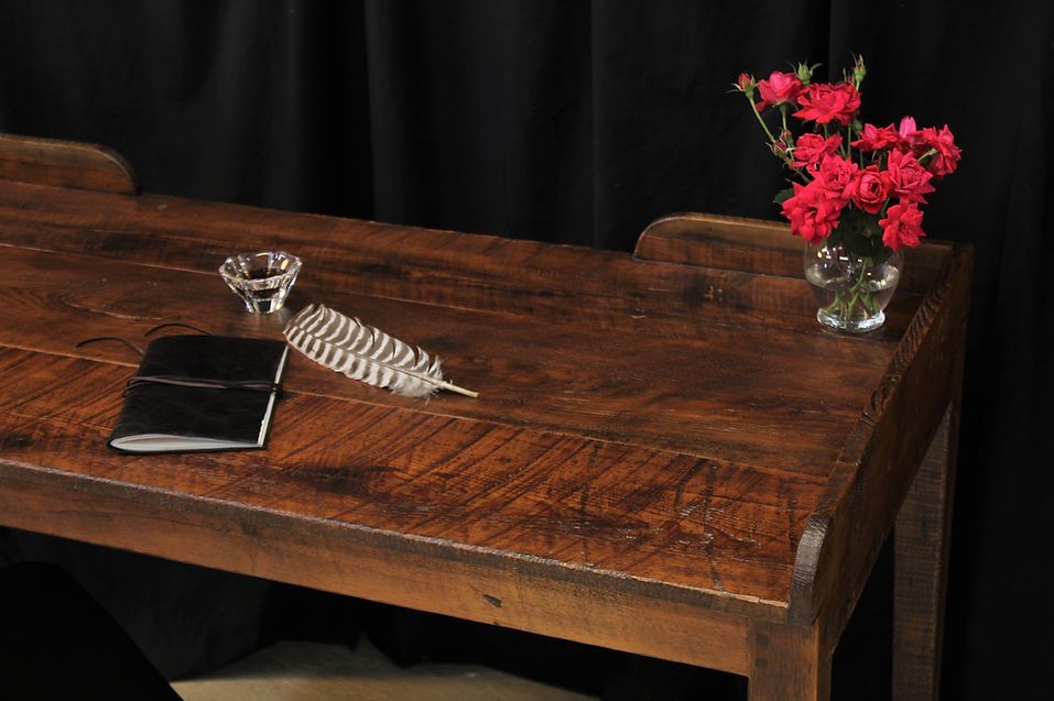 Wooden desk with a black notebook, quill, inkwell, and pink flowers in a vase