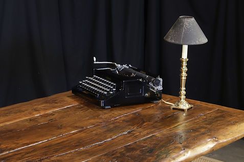 Black typewriter and brass lamp on a wooden desk against a black backdrop