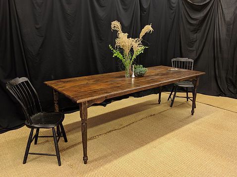 Long wooden table with two black chairs, and vase of flowers against black backdrop