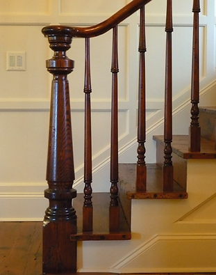 Wooden staircase with dark brown railing, balusters, and newel post