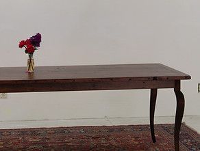 Wooden table with flowers in a vase on top, set on a rug against a white wall
