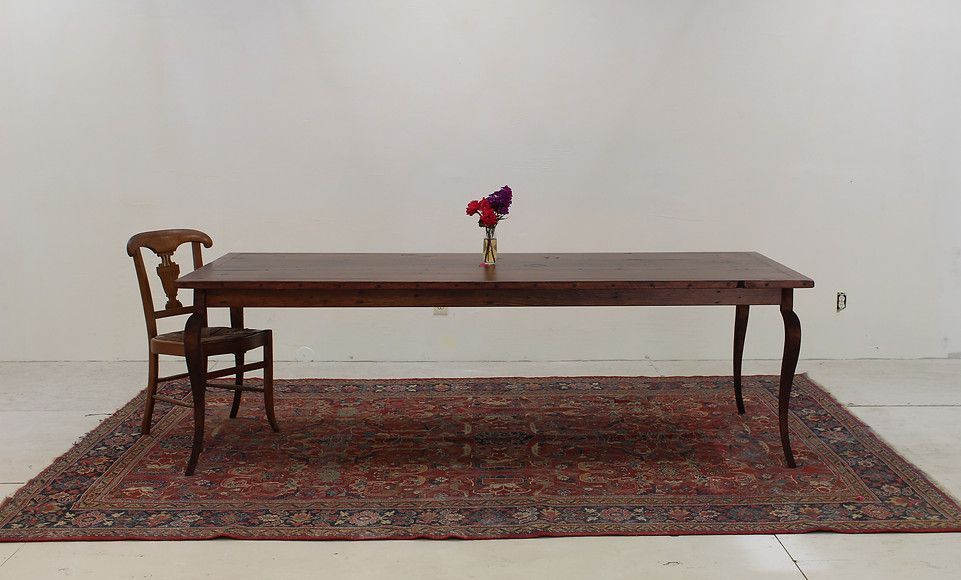 Wooden table with vase of flowers, chair, and patterned rug in a white room