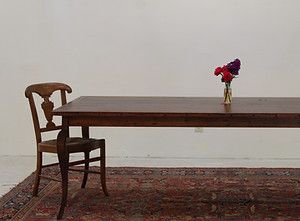 Wooden chair beside a long brown table with vase of flowers on an oriental rug