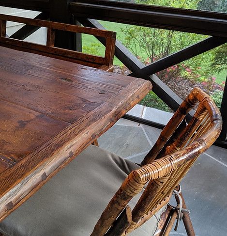 Wooden table and chair on a patio with a view of greenery through a black railing