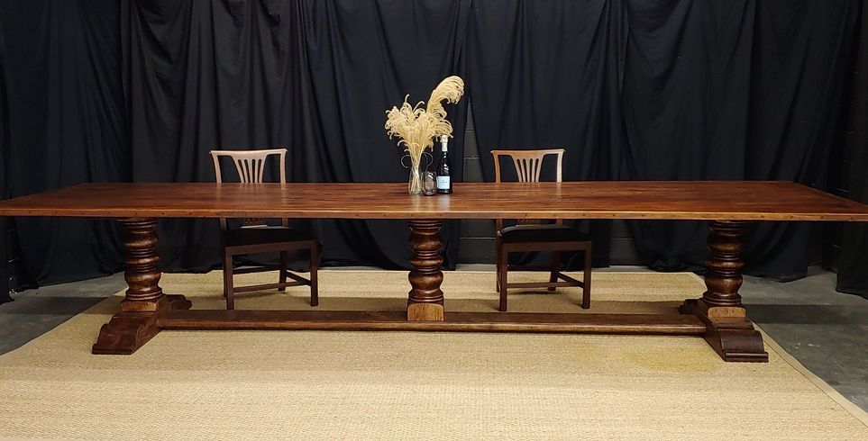 A long, wooden dining table with two chairs and dried flowers against a dark backdrop