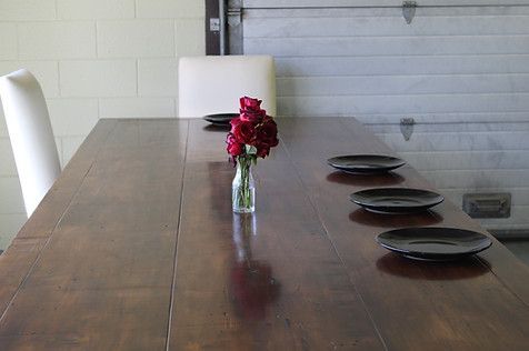 Dining table set with black plates, a vase of red flowers, and white chairs