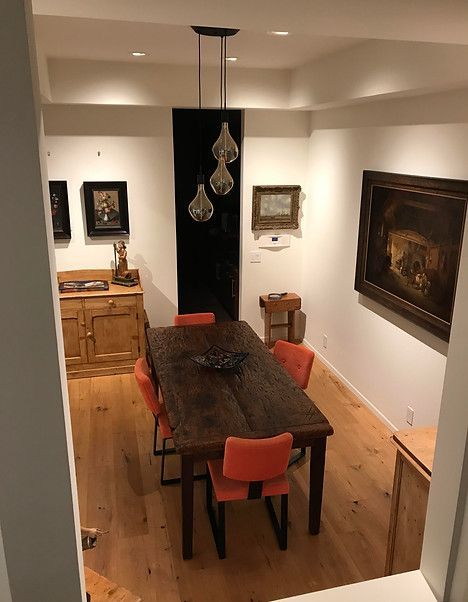 Dining room with wood table, orange chairs, art on walls, and a hanging light fixture