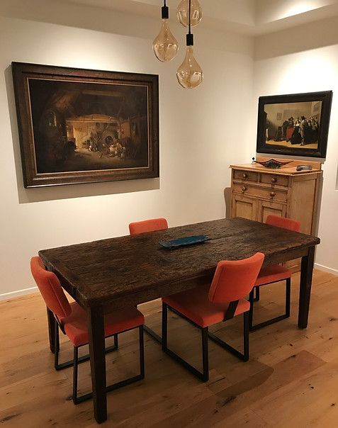 Dining room with wooden table, orange chairs, artwork on the walls, and pendant lights