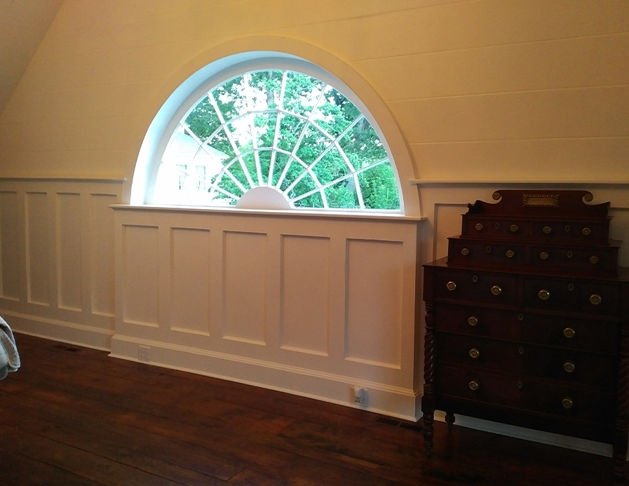 White paneled wall with arched window and dark wood chest of drawers
