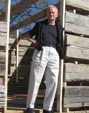 Man in black jacket and white pants, standing in front of wood beams